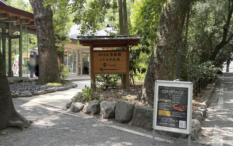 くさなぎ広場への案内看板。奥に「剣の宝庫 草薙館」の建物が見える。